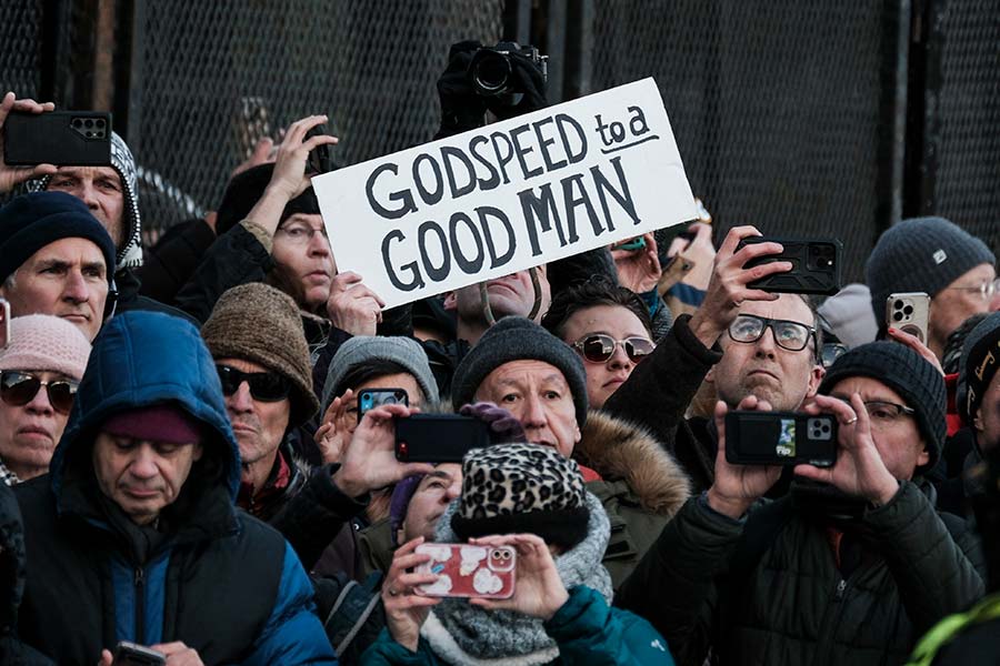 Onlookers hold a sign reading 'Godspeed to a Good Man'