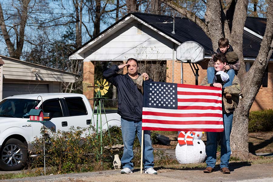 A three-person family salutes from a yard.