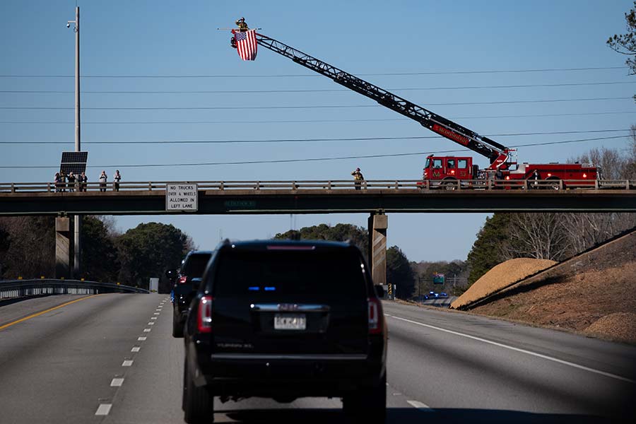 Firefighters salute from truck ladder basket.