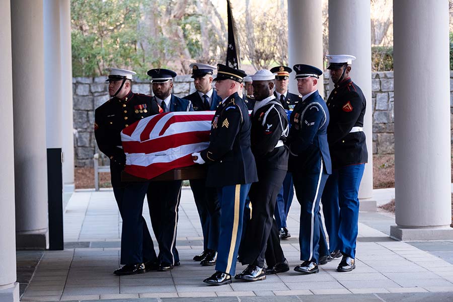 Military personnel carry flag-draped casket.