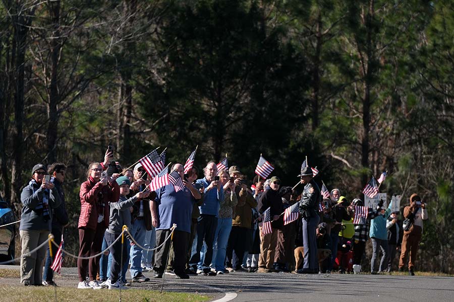 Mourners stand along the roadside.